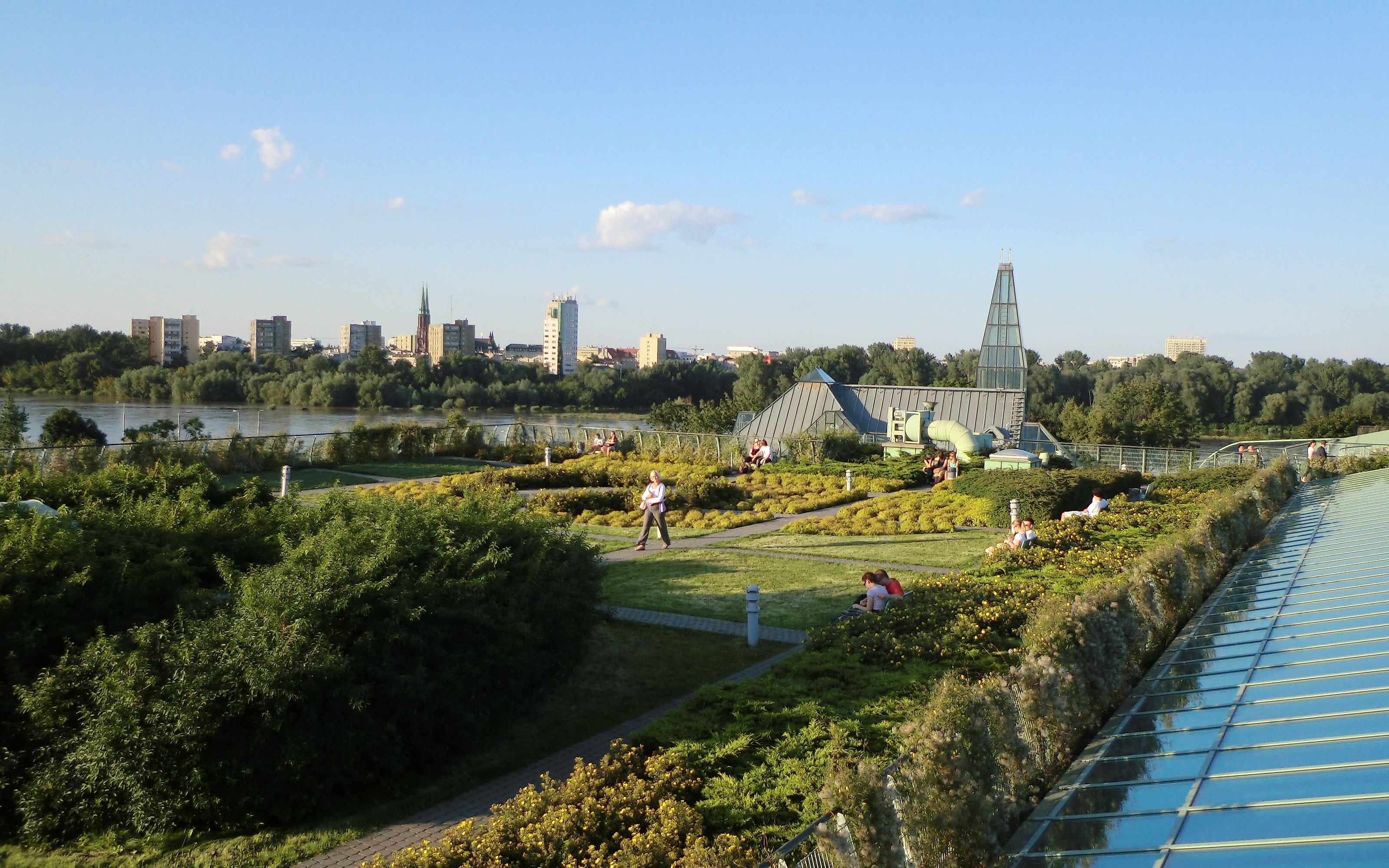 People sitting on benches on a large roof garden with lawn, shrubs and bushes.